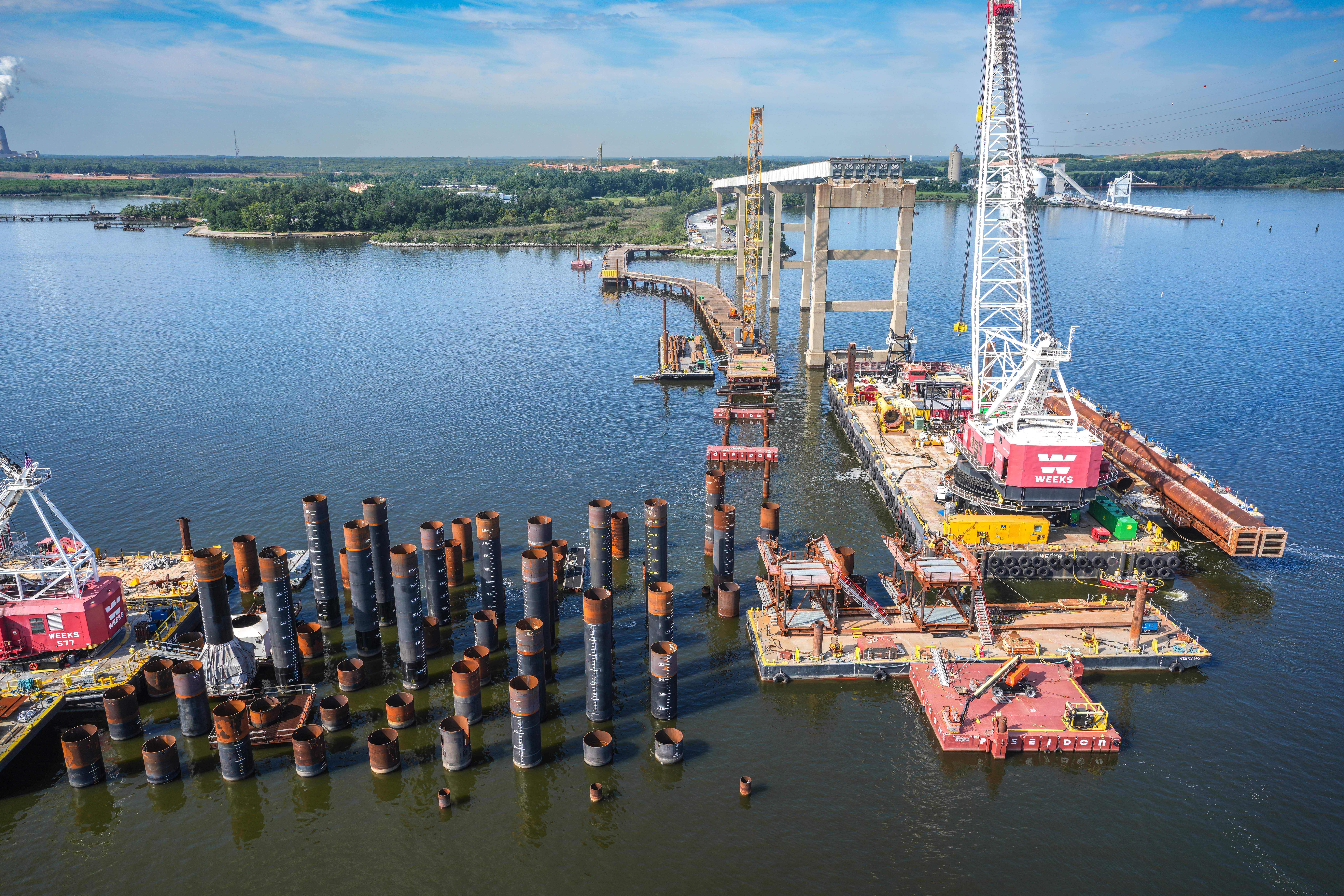 Aerial view of crane on barge and bridge piles in water.